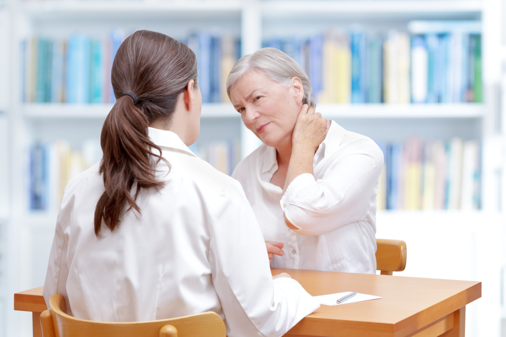 Senior female patient consulting her physician or doctor on account of chronic neck pain caused