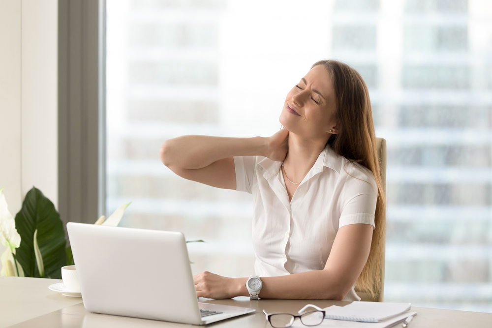 Businesswoman feeling pain in neck after sitting at the table with laptop.