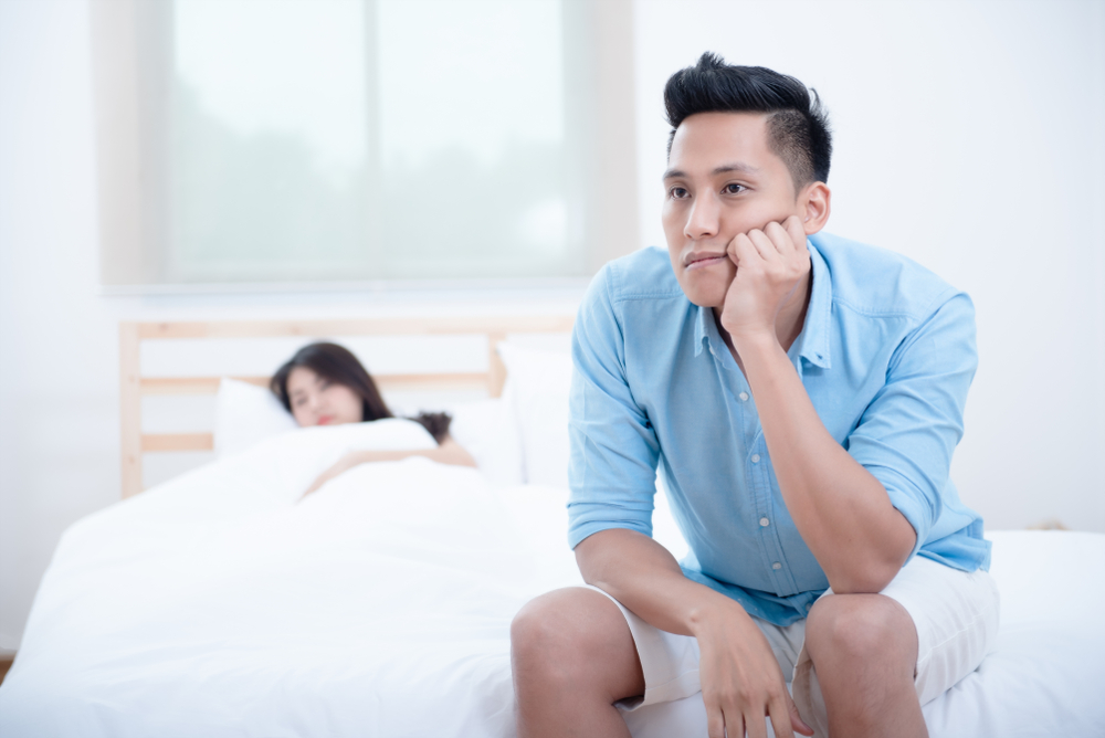 Husband unhappy and disappointed in the erectile dysfunction during sex while his wife sleeping on the bed