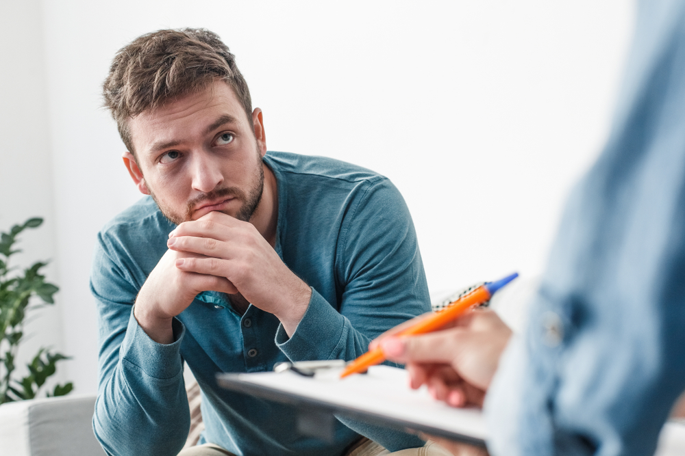 Man sitting down while doctor holding a notepad talks to him